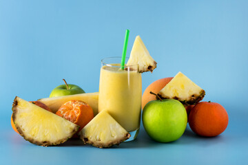 Naklejka na ściany i meble Freshly Blended Yellow and Orange Fruit Smoothie in Glass with Straw Pineapple and Citrus Smoothie Healthy Drink Blue Background Horizontal