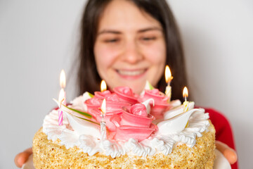 A brunette woman in red clothes holds a large white cake with candles, makes a wish