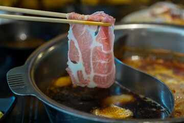 chopsticks take beef slice into shabu shabu pot, healthy food. Japanese cuisine, Japanese beef shabu-shabu on wooden table. Sukiyaki in the marbled Japanese beef.