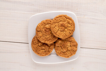 Several sweet homemade cookies with a white ceramic saucer  on a wooden table, close-up, top view.