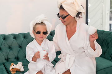 Mother with child doing beauty treatment together. Happy family mother and child daughter in towel and bathrobe are sitting on the couch. beauty salon concept, wellness spa, Long banner format