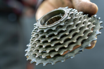 A bicycle mechanic in the workshop holds a cassette from a mountain bike in his hands. Bicycle repair and replacement of worn parts. Broken parts close-up.