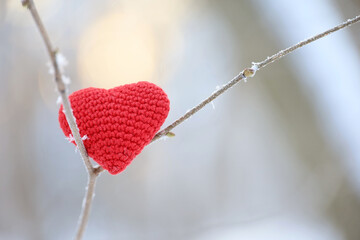 Red knitted love heart on a tree twig covered with snow and frost in winter forest. Valentine's card, background for Christmas celebration