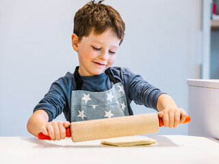 Cute boy kneading dough with rolling pin