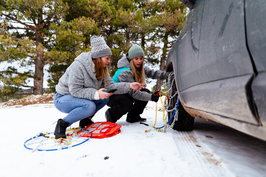 Women friends trying to put snow chain on wheel tire