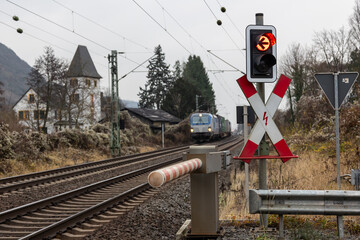 A freight train with an electric locomotive passing a level crossing signal with a red warning light