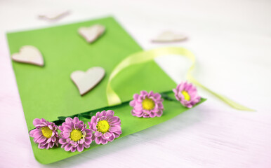 Bright green envelope with pink chrysanthemum flowers and decorative wooden hearts lies on a white table
