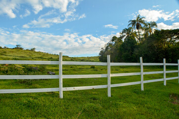 Fototapeta na wymiar white fence on green field with blue sky
