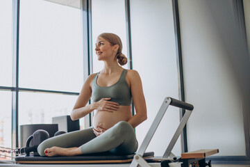 Pregnant woman exercising with the help of reformer on pilates class