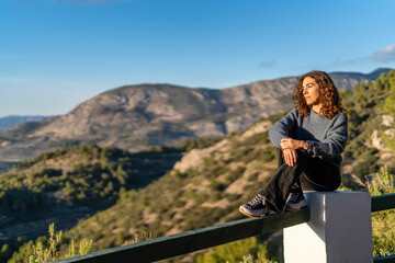 Naklejka premium Woman sitting on railing looking at mountains on sunny day in nature
