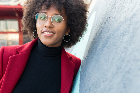 Stylish black woman with curly hair wearing coat and eyeglasses