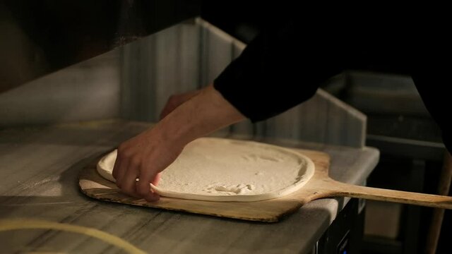 A slow motion of hands, stretching the pizza dough on a wooden board and then pouring onion spread on the dough, minutes before it enters the oven. Israel.