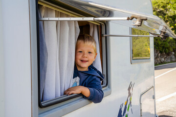 Happy small boy looking through the RV's window parked along the road