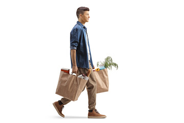 Full length profile shot of a guy carrying grocery bags and walking - obrazy, fototapety, plakaty