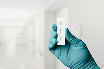 Gloved hand holding a rapid test device for COVID-19 with negative test result. 