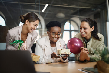 Happy African American businesswoman blowing candle on Birthday cake while having party with her colleagues in office.