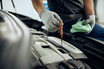 Close-up of auto repairman checks oil level during engine maintenance in workshop.