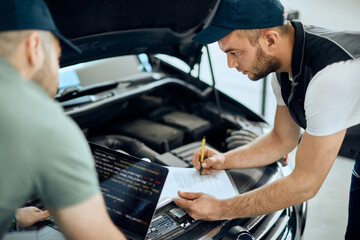 Two mechanics cooperate while doing car engine diagnostic at auto repair shop.