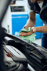 Close-up of mechanic wipes his dirty hands after working on car engine at repair shop.