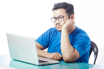 young man sitting in front of a laptop with sad expression wearing glass