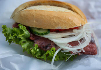 Ein mit frisch geräucherten Fisch, Salat und Zwiebeln belegtes Brötchen.
