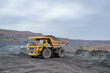 A large yellow dump truck unloads minerals. The process of mining and transportation of minerals. Ore mining by open-pit method.