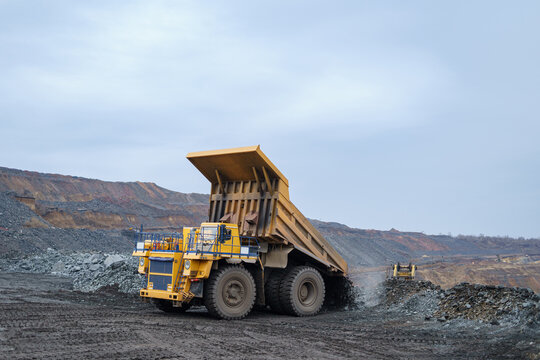 A large yellow dump truck unloads minerals. The process of mining and transportation of minerals. Ore mining by open-pit method.