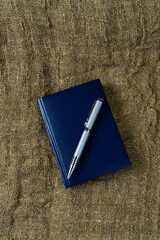 A blue notebook and an office silver pen lie on a rough gray cloth. Stationery on old yellowed...