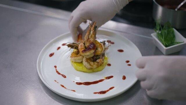 High angle view plate with cooked prawn and male hand adding strawberry in slow motion. Unrecognizable Caucasian male chef decorating dish serving food in restaurant kitchen
