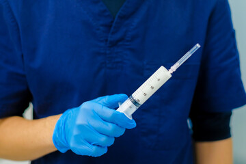 A doctor's hand in a sterile glove close-up holds a large white syringe. Selective focus.