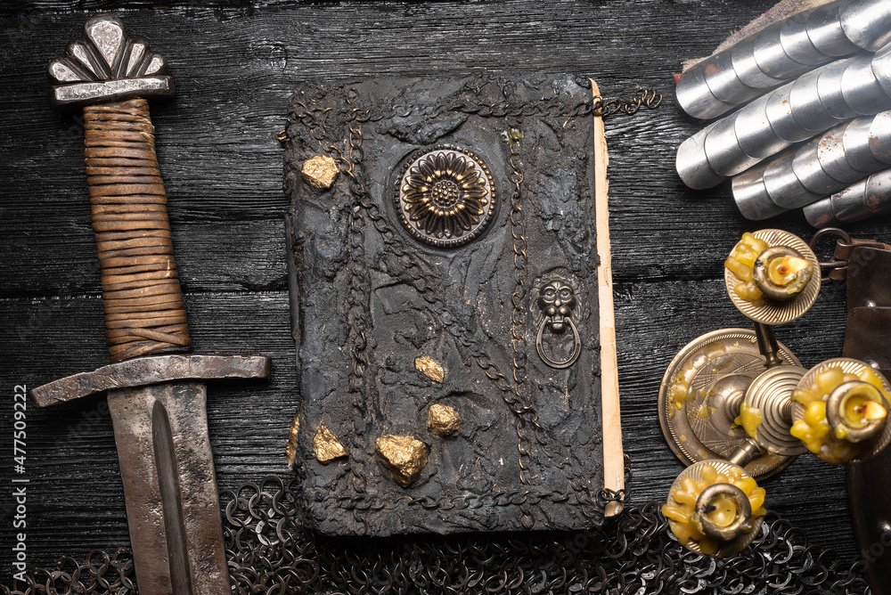 Wall mural Ancient story book and knight sword on the old wooden table background with copy space. Medieval concept.