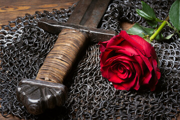 Red rose flower and knight sword on the black table background close up.