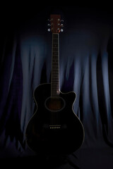 low key image of the silhouette of an acoustic guitar on a stage with a lightly illuminated black...
