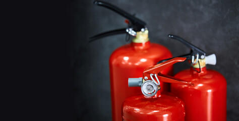 Three red fire extinguishers on a dark background with the space for text. 