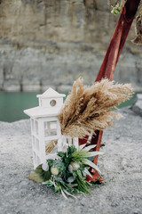 white wooden candlestick in boho style near which green leaves and dried flowers, reeds, pampas grass on the ground