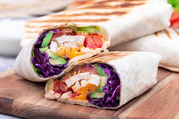 Grilled chicken wraps with red cabbage, avocado, tomato, lettuce and cheddar cheese, on wooden board