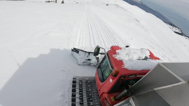 Snowcat ratrack with snowplow preparing the ski slope, driving through the deep snow piste in the ski resort. Heavy machinery transport free style skiers on mountain peak