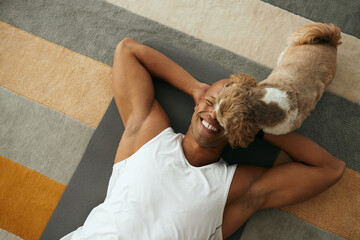 Above view of happy black athlete and his dog at home.
