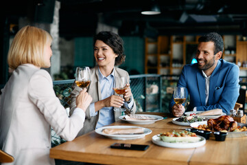 Happy businesswoman drinks wine and talks to her colleagues during lunch in restaurant.