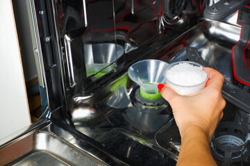 Adding salt to the dishwasher. A woman's hand pours salt to soften the water into the dishwasher. Dishwasher salt for regenerating the water softener