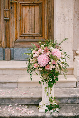 Fototapeta na wymiar Bouquet of roses, hydrangeas and ivy stands on a small column on the stone steps of the church