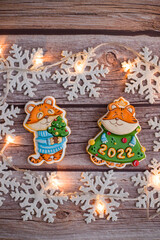 Vertical gingerbread house, car and tiger symbol of the year 2022. The tiger is the symbol of the year 2022. Beautiful Christmas gingerbread cookies on a wooden background with lights and snowflakes.