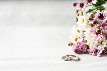 Pair of wedding rings on a white surface with beautiful white and purple flowers on the edge....
