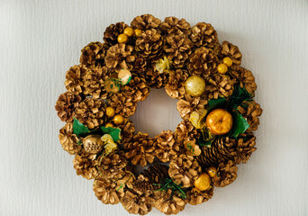 A Christmas wreath made of natural fir and pine cones hanging on a white wall. New Year and winter holidays.