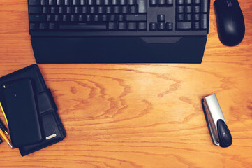 Workplace. On a wooden table are located: keyboard, computer mouse, smartphone, card holder, pencils and a stapler.