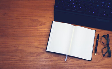 Workplace. On a wooden table are located: keyboard, glasses, notebook and pen.