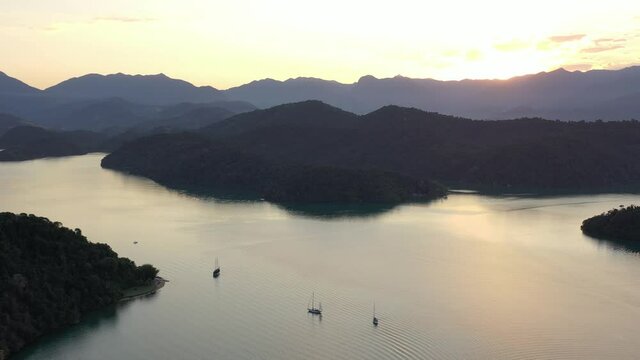 Sailing boats anchoring before sunset, on calm waters between tropical islands of the coast of Paraty, Rio de Janeiro