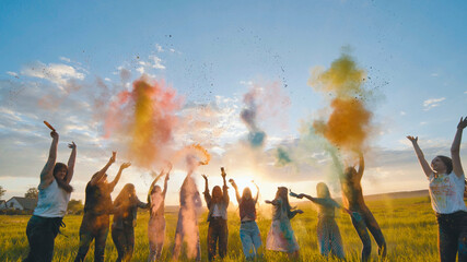 Cheerful girls toss up multi-colored powder at a beautiful sunset.