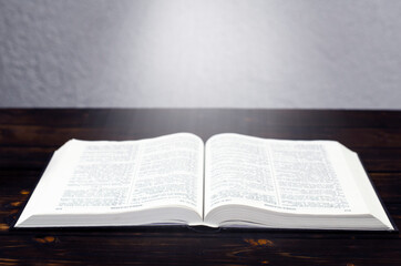 Open Bible book, on a wooden table. Desk lamp. Light from a book