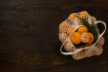Fresh mandarin oranges fruit or tangerines on a wooden table. Christmas composition. Mandarin oranges in organic cotton mesh bag. Grocery shopping fabric net bag. No plastic bag. - 477521803